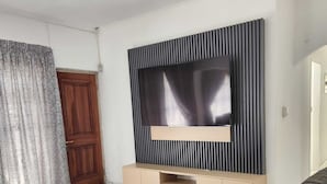 A modern living room with a flat-screen TV mounted on a wall, a dark leather sofa, and a wooden door.