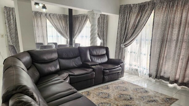 A modern living room with a sectional sofa, a patterned rug, and large windows with curtains.