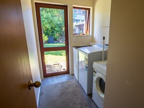 A laundry room with a washing machine, dryer, and a small window with a view of a yard.