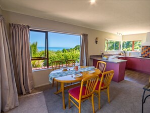 A dining area with a table and chairs, a kitchen with a counter and sink, and a view of the sea through large windows.