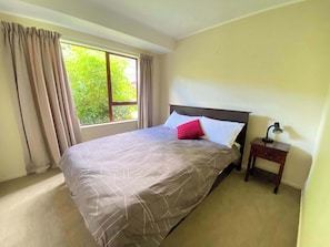 Ein Schlafzimmer mit einem großen Bett, einem Nachttisch, einer Lampe und einem Fenster mit Vorhängen.