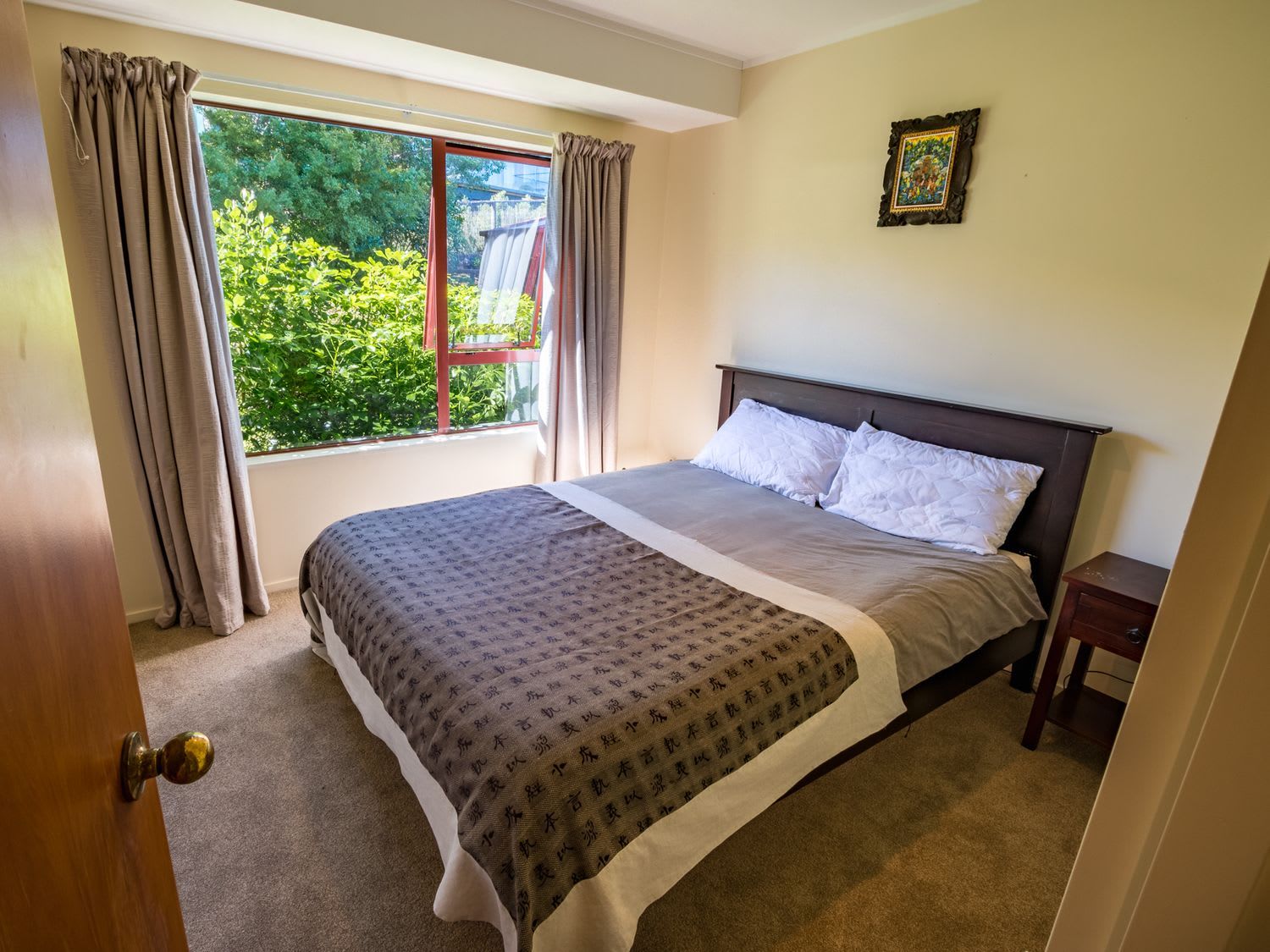 A bedroom with a bed, a window with curtains, a bedside table, and a picture on the wall.