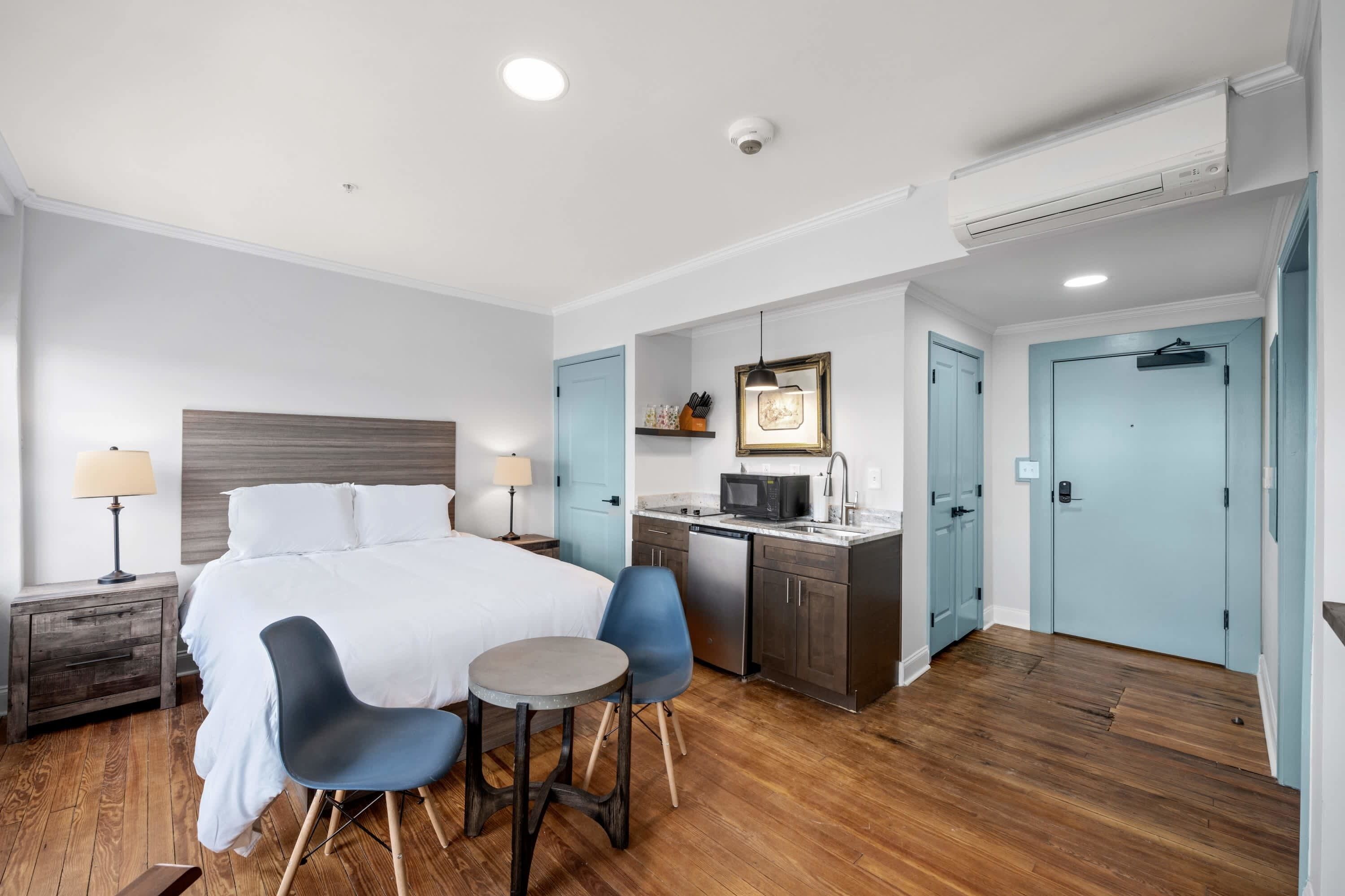 A hotel room with a bed, two chairs, a small table, a microwave, a sink, and a wardrobe.