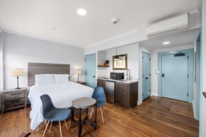 A hotel room with a bed, two chairs, a small table, a microwave, a sink, and a wardrobe.