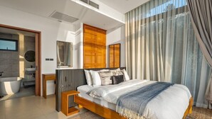 Un dormitorio moderno con una cama grande, cabecera de madera, mesita de noche, espejo y vista al baño.