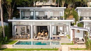 Una casa moderna de dos pisos con piscina, mobiliario exterior y un muro de piedra.