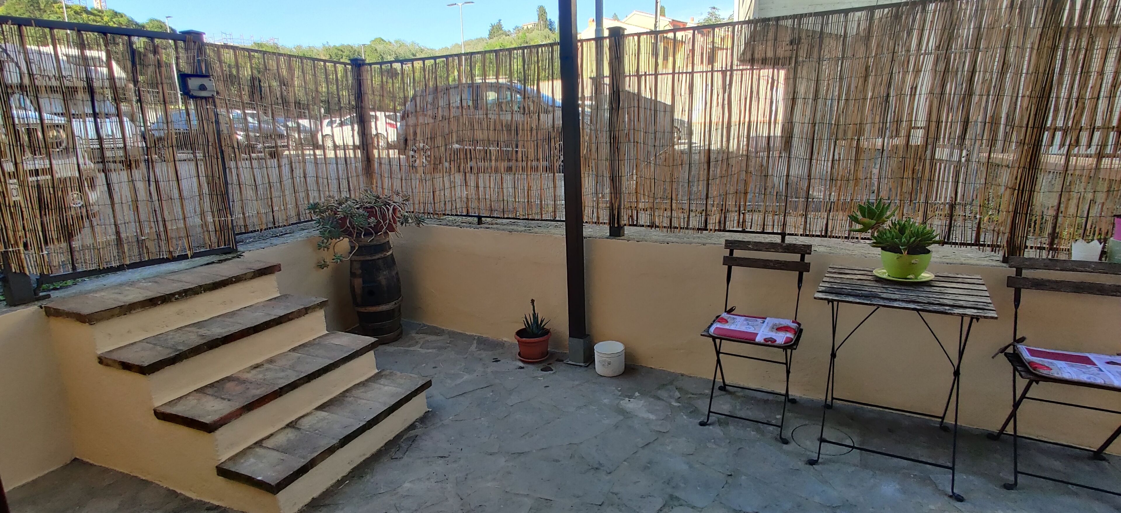 A balcony with steps leading to a small outdoor area, a table with chairs, and potted plants.