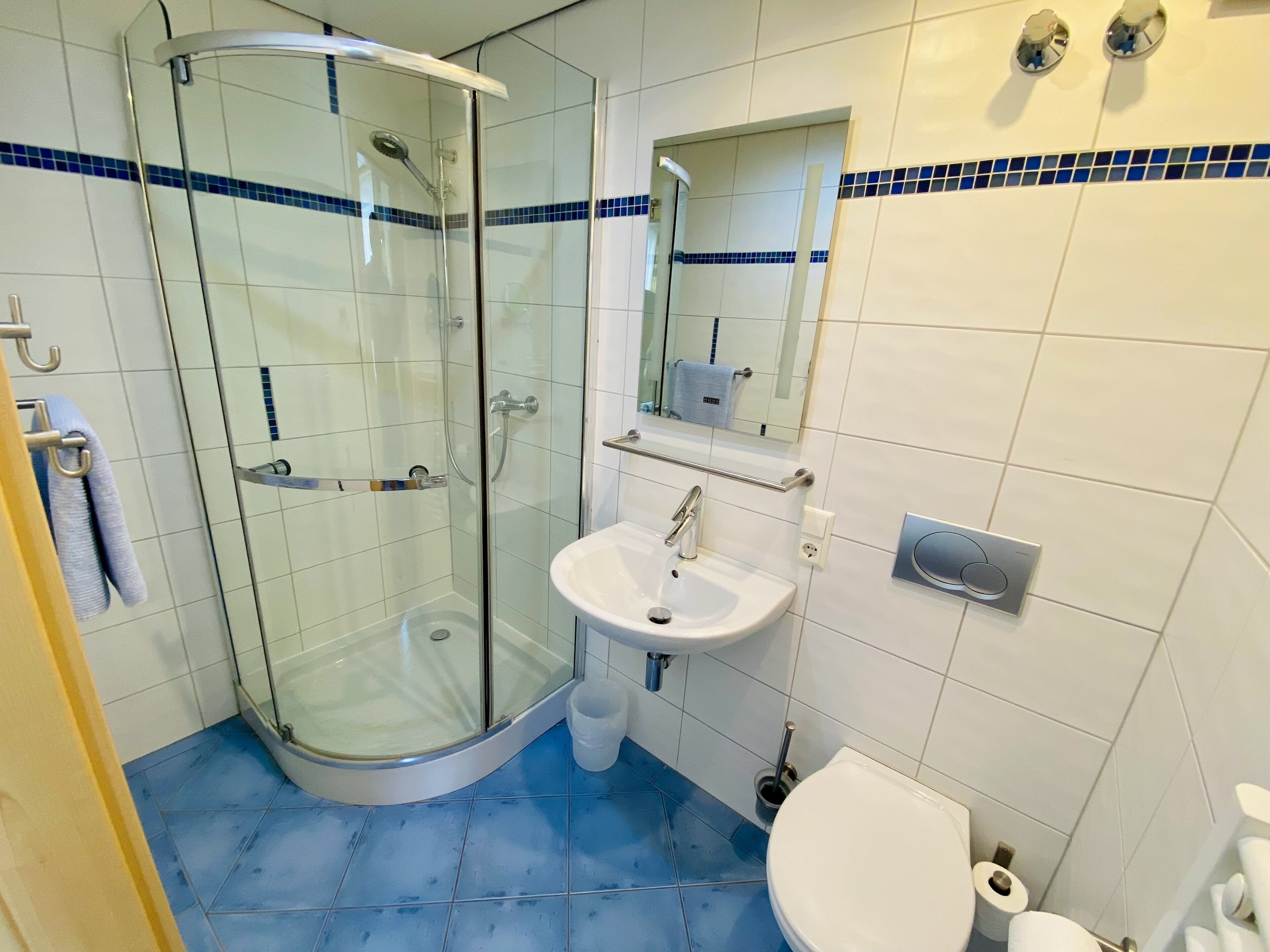Ein Badezimmer mit einer Duschkabine, einem weißen Waschbecken, einer Toilette und einem Spiegel über dem Waschbecken.