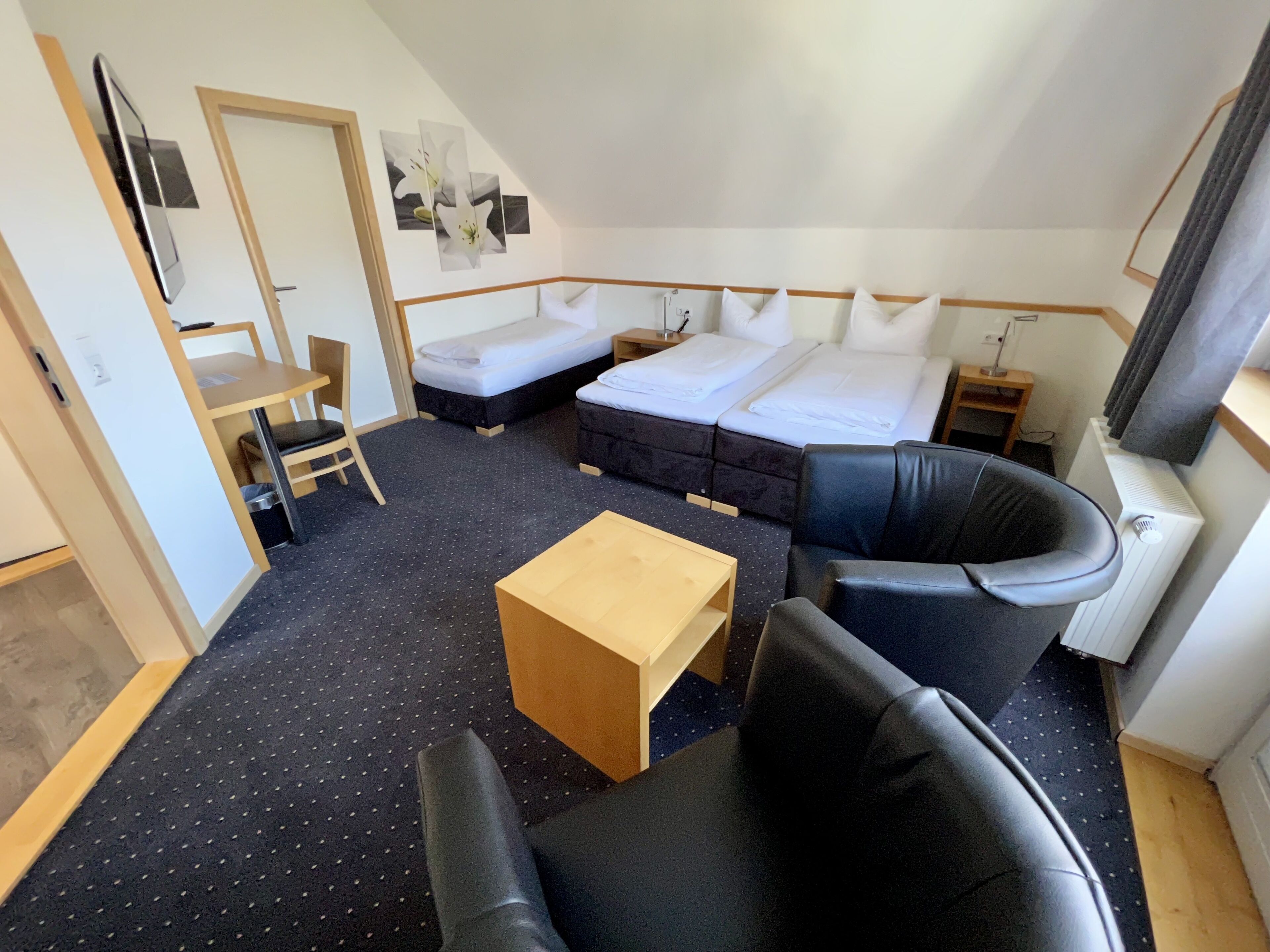 A hotel room with a bed, a sofa, a small table, and a TV.