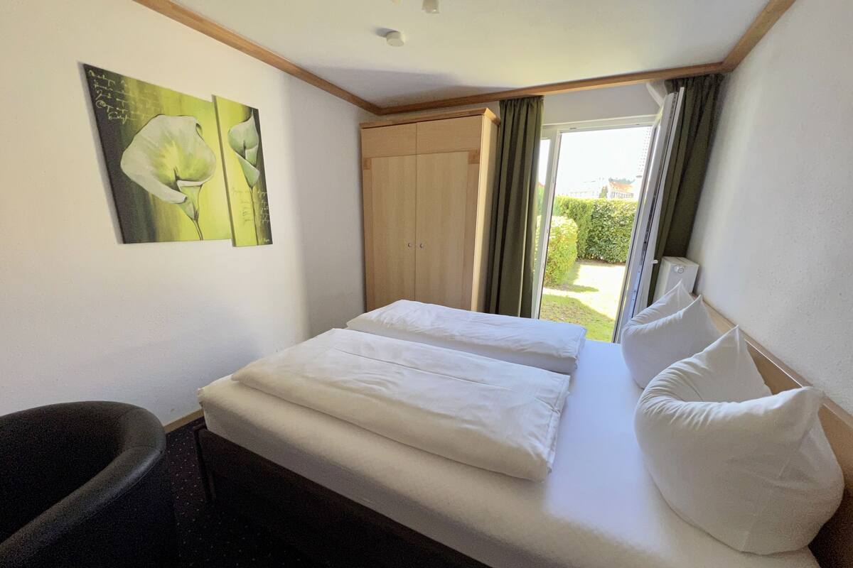 Ein Hotelzimmer mit einem Bett, einem Sessel, einem Gemälde und einem Fenster mit Vorhängen.