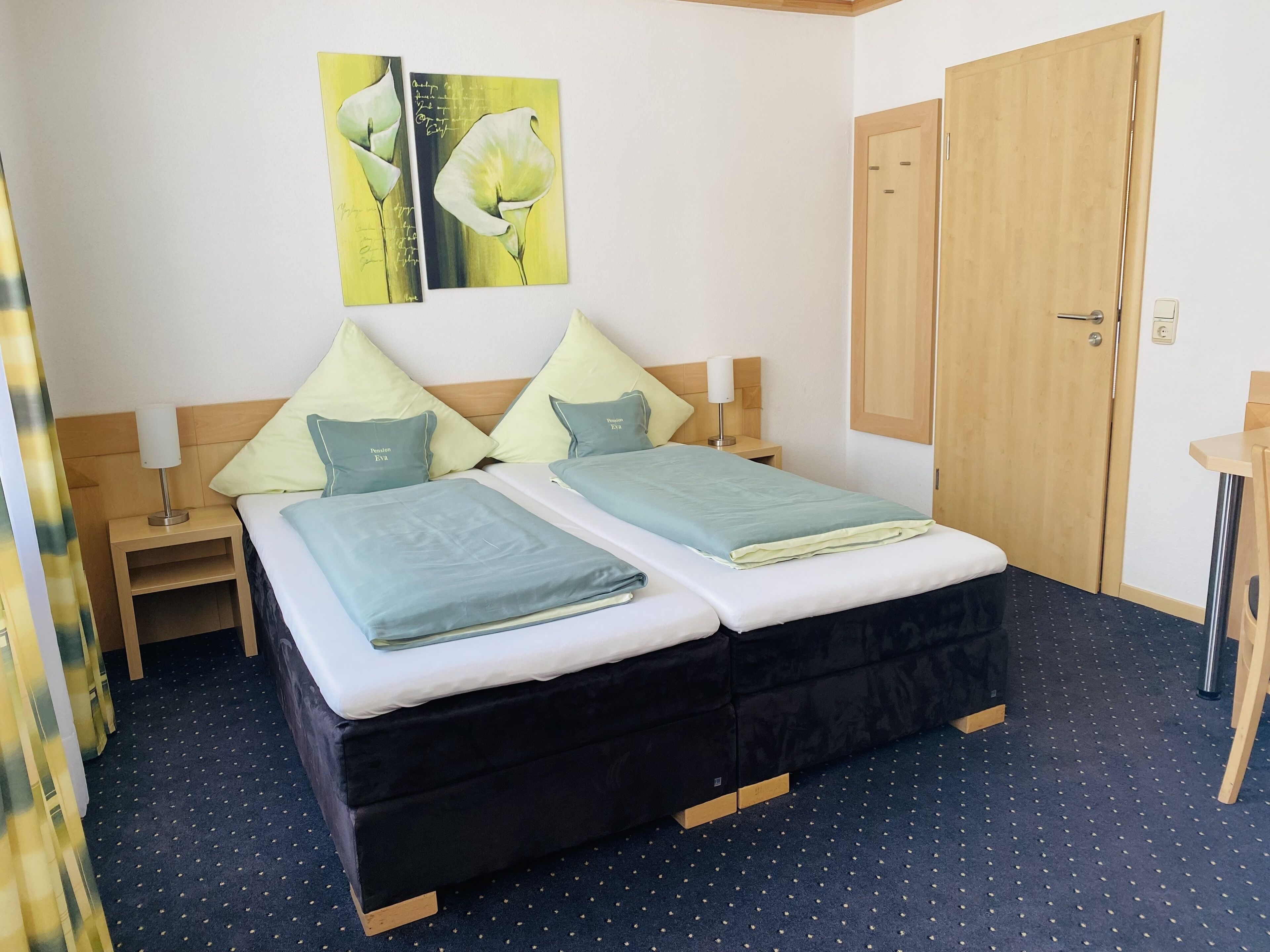 A double bed with two pillows, a bedside table with a lamp, and a wooden wardrobe.
