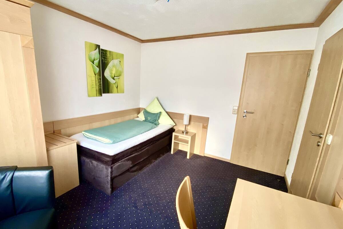 Ein kleines Zimmer mit einem Bett, einem Schreibtisch, einem Stuhl und einem Kleiderschrank.