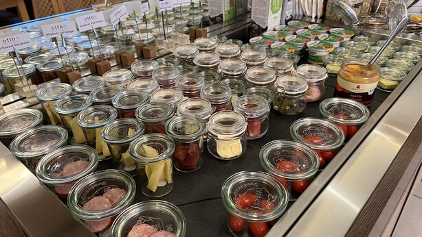 Un bufé con diversos alimentos en recipientes de vidrio, como carnes, quesos y vegetales.