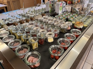Un bufé con diversos alimentos en recipientes de vidrio, como carnes, quesos y vegetales.