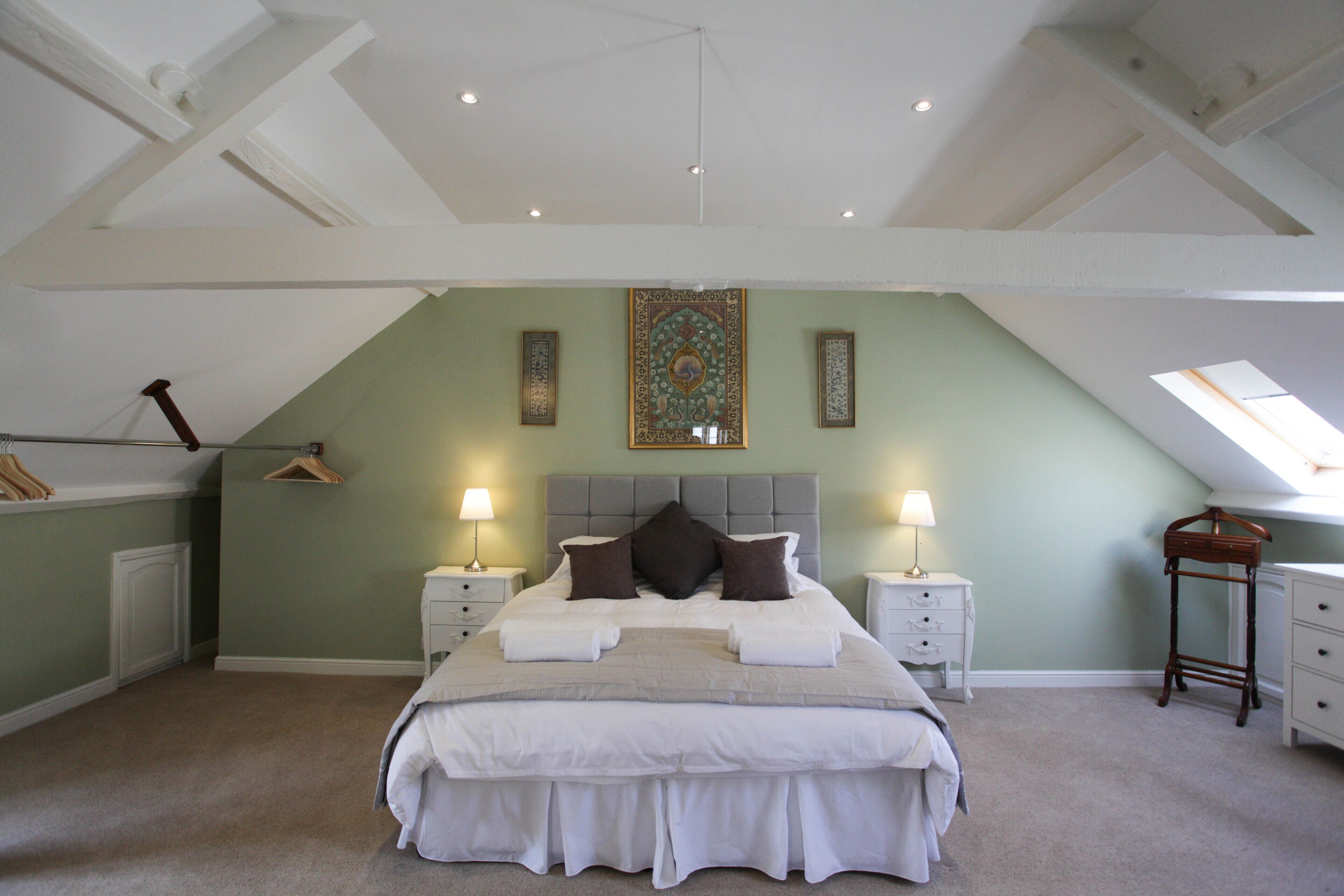 Une chambre avec un grand lit, deux tables de chevet avec des lampes, un porte-vêtements et une petite table avec une chaise.