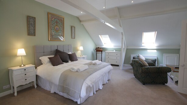 A bedroom with a large bed, two bedside tables, a chair, and a skylight. - Thistlebank Townhouse  (Whitby)