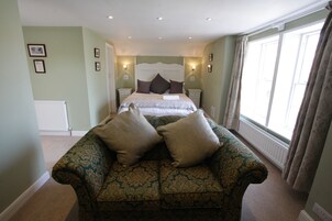 A bedroom with a large bed, two bedside tables, a patterned sofa, and a window with curtains.
