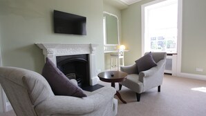 A living room with a fireplace, two armchairs, a round table, and a television mounted on the wall. - Thistlebank Townhouse  (Whitby)