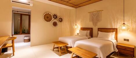 Une chambre avec deux lits, une table en bois, un banc et un luminaire suspendu.