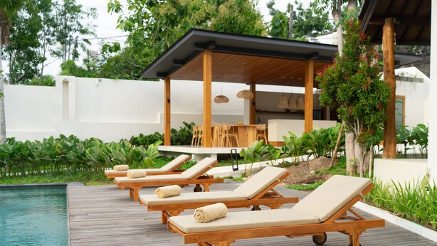 Un área junto a la piscina con sillones de madera y una zona de estar cubierta.