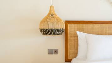 Une chambre avec une table de chevet en bois, un lit avec une literie blanche, une suspension en fibres tressées et une décoration murale en macramé.