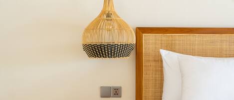 A bedroom with a wooden nightstand, a bed with white bedding, a woven pendant light, and a macrame wall hanging.