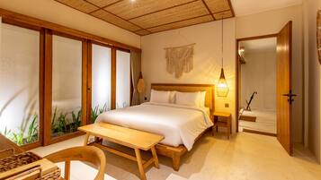 A bedroom with a large bed, wooden furniture, a bedside table, a hanging light fixture, and a view through a sliding door.