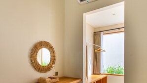 Una habitación moderna y minimalista con un escritorio de madera, un espejo redondo y un equipo de aire acondicionado.