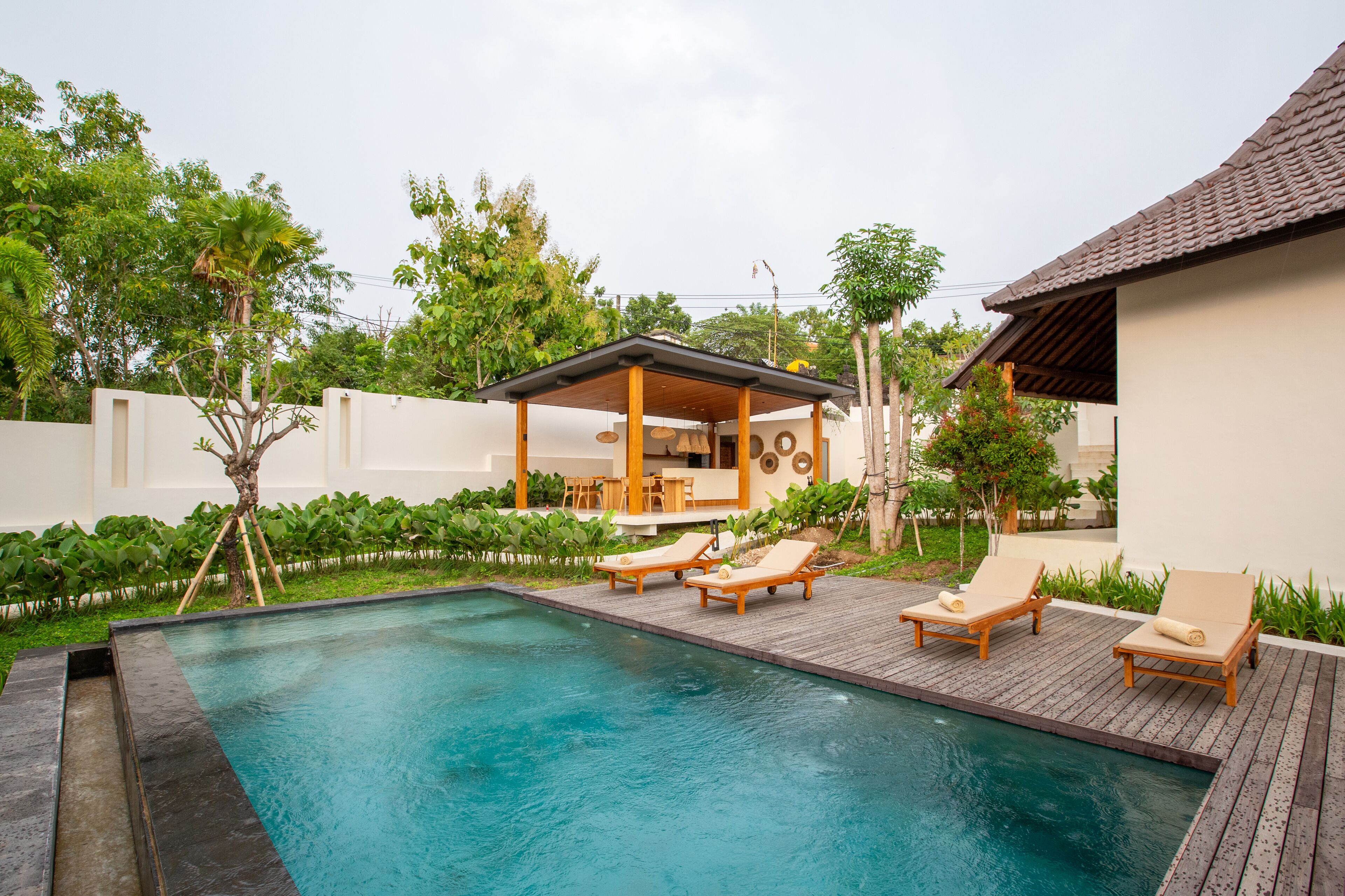A swimming pool with lounge chairs, a covered seating area, and a white building with a tiled roof.