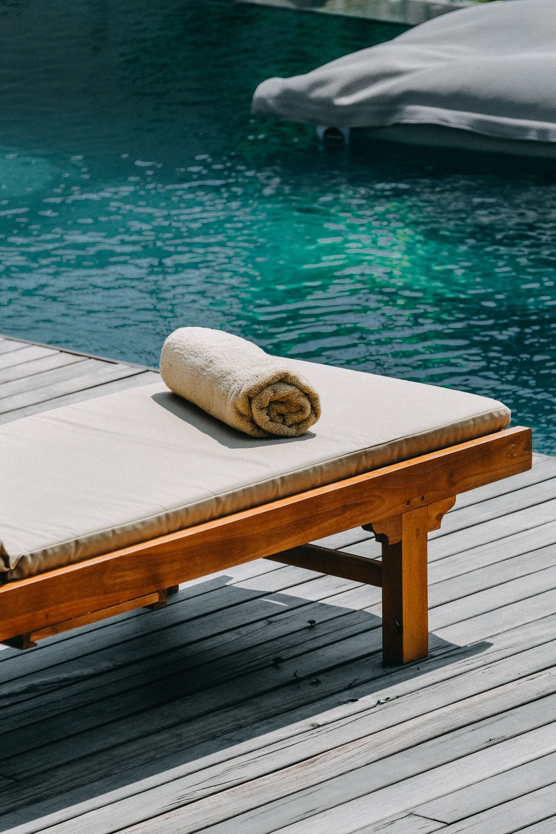 Una terraza de madera con una silla de salón y una toalla enrollada.