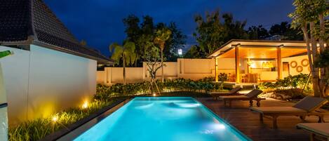 A swimming pool with lounge chairs and a well-lit outdoor area at dusk.