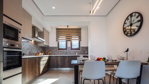 A modern kitchen with built-in appliances, a dining area with two chairs, and a large wall clock. - Riviera Vista Luxury Homes, Mousela 2broom suite with sea view and shared pool (Dramia)
