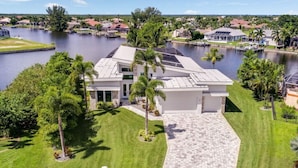 A modern house with a paved driveway, surrounded by lush greenery and a body of water. - Villa Rapa Nui Island (Cape Coral)