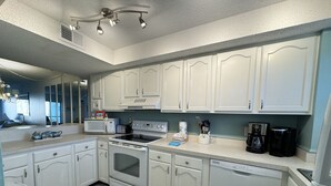 A kitchen with white cabinets, a stove, microwave, and coffee maker.