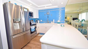 A modern kitchen with stainless steel appliances, white cabinets, and a blue backsplash.