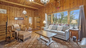 A cozy log cabin interior with a wooden floor, a sofa, a coffee table, and a chandelier. - Hidden Pines -- Ev#3034 2 Bedroom Home by RedAwning (Estes Park)