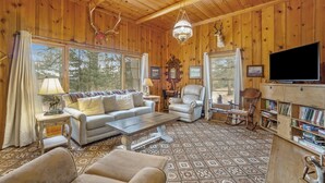 A cozy cabin interior with a sofa, armchairs, a coffee table, a TV, and a bookshelf. - Hidden Pines -- Ev#3034 2 Bedroom Home by RedAwning (Estes Park)