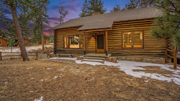 A log cabin with a stone-paved entrance, surrounded by trees and snow patches. - Hidden Pines -- Ev#3034 2 Bedroom Home by RedAwning (Estes Park)