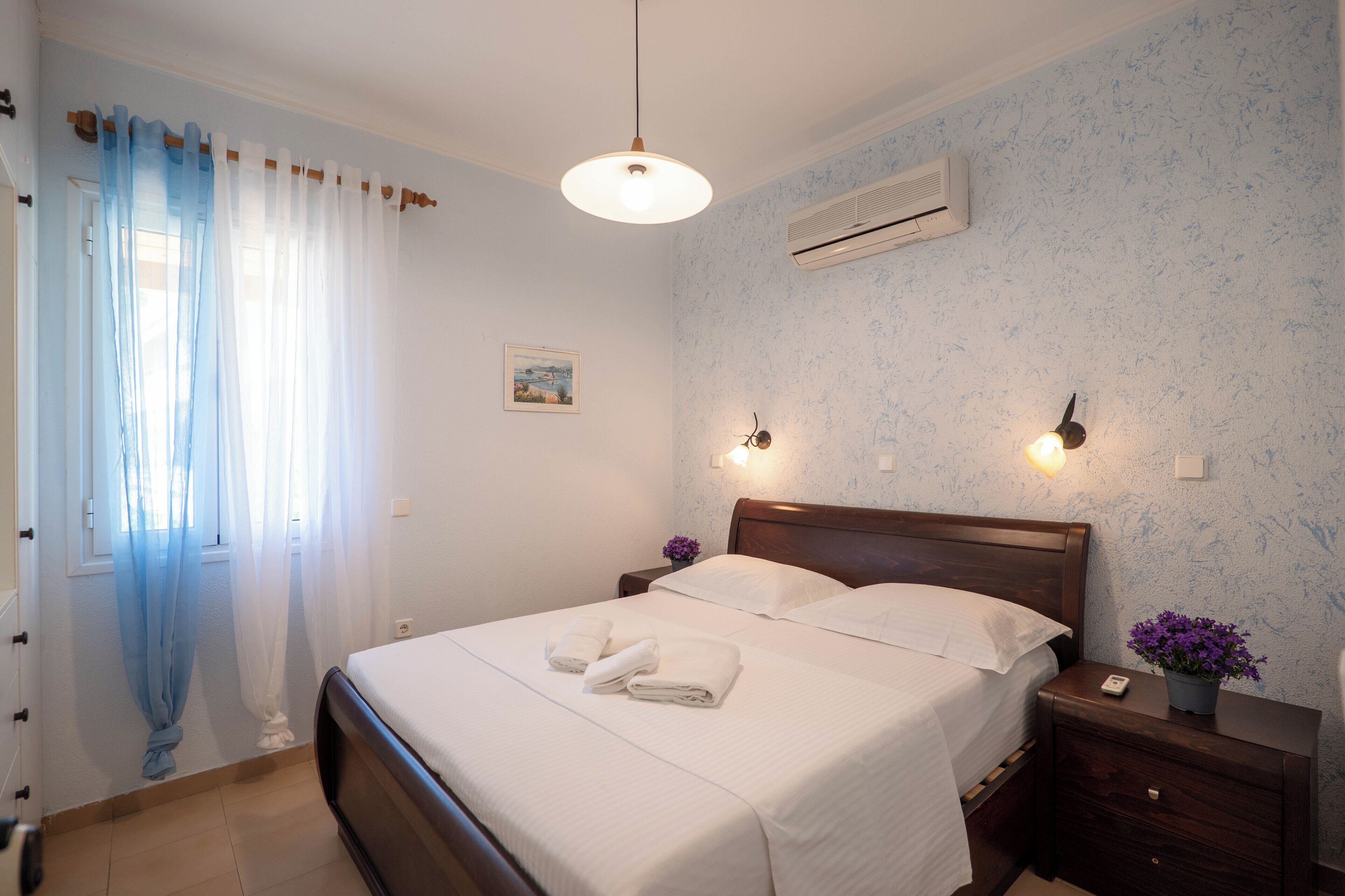 A bedroom with a bed, bedside tables, a nightstand, an air conditioner, and a window with curtains.