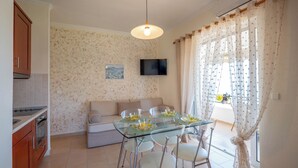 A modern kitchen with a dining area, a sofa, and a TV mounted on the wall. - Corfu Glyfada Menigos Resort 86 (Corfu)