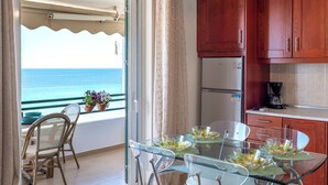 A balcony with a view of the sea, a glass table with clear glassware, wooden cabinets, and a refrigerator. - Corfu Glyfada Menigos Resort 86 (Corfu)
