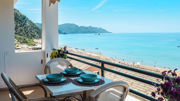 A balcony with a table set for dining, overlooking a beach and the sea. - Corfu Glyfada Menigos Resort 86 (Corfu)