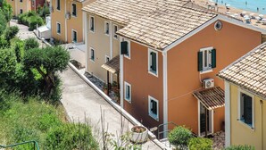 A coastal village with terracotta-roofed buildings, a clear blue sea, and a hilly backdrop. - Corfu Glyfada Menigos Resort 86 (Corfu)
