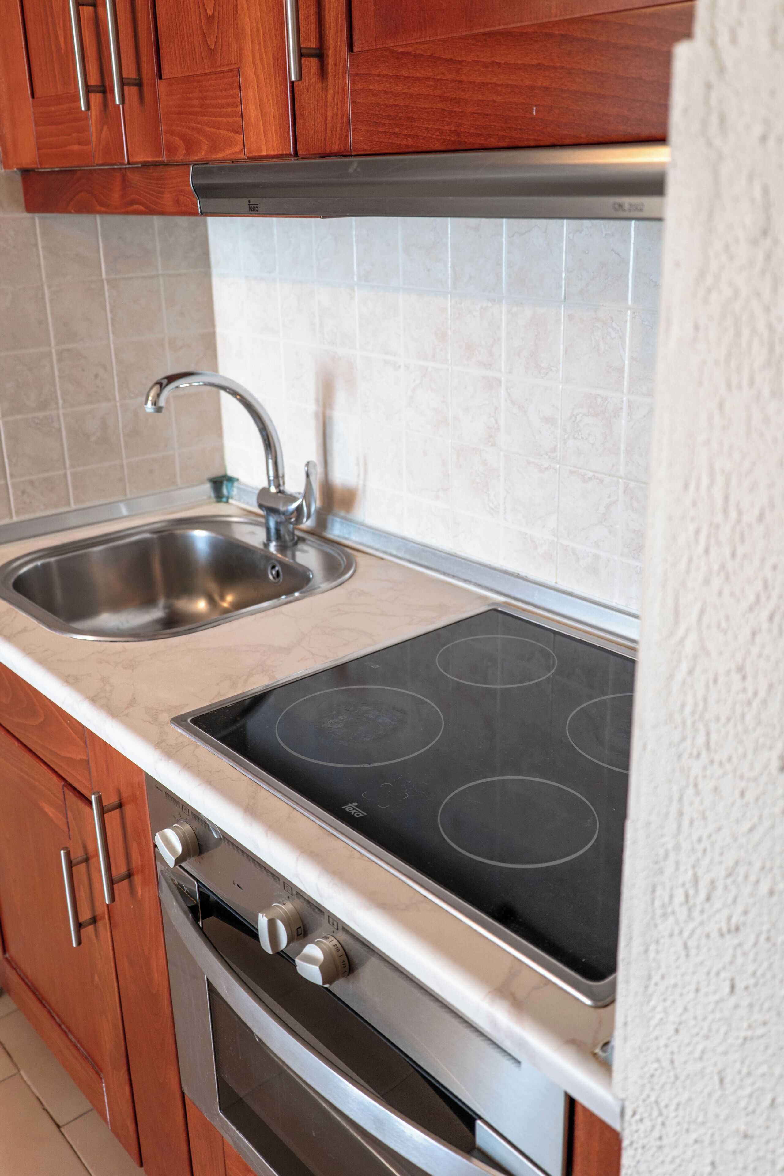 Een keuken met houten kastjes, een roestvrijstalen spoelbak, een geïntegreerde kookplaat en een oven.