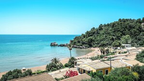 A coastal village with terracotta-roofed buildings, a beach, and a clear blue sky. - Corfu Glyfada Menigos Resort 86 (Corfu)