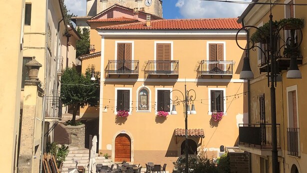 A narrow street with a building featuring a clock tower, balconies with flower boxes, and outdoor seating. - Stunning 3-bed House in Gallinaro, Aircon and Pool (Gallinaro)