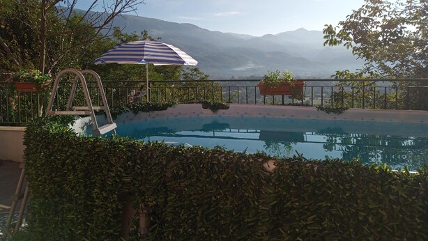 Une piscine avec vue sur les montagnes, un fauteuil de relaxation et un parasol à rayures.