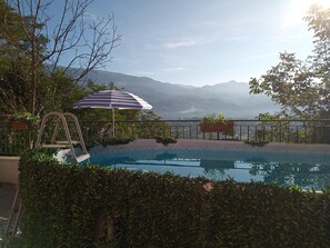 A pool with a view of mountains, a lounge chair, and a striped umbrella. - Apartment With Air-con and Pool (Gallinaro)