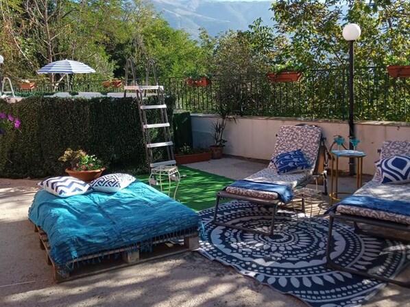 A rooftop terrace with a bed, lounge chairs, and a patterned rug.