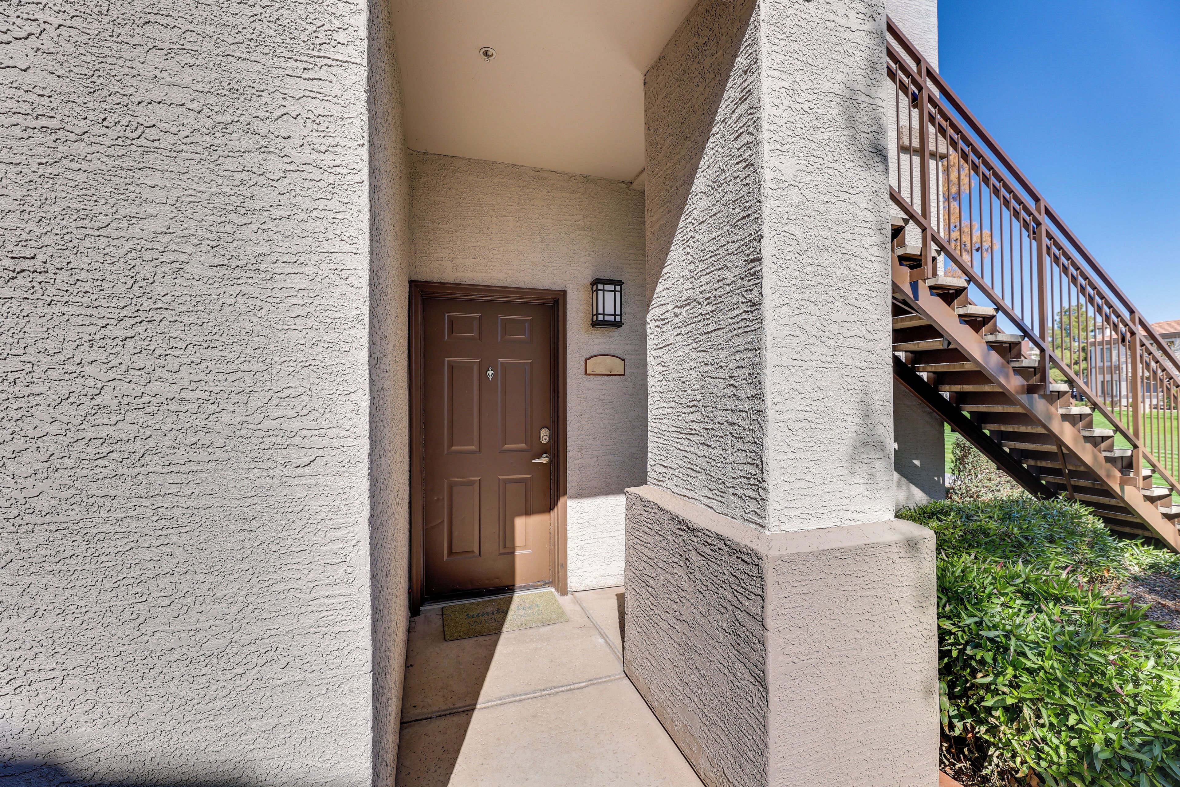 A building entrance with a brown door, a small outdoor light fixture, and a wooden staircase.